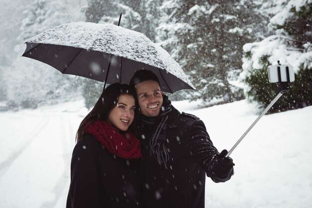 Casal sorridente tirando uma selfie no celular durante a queda de neve