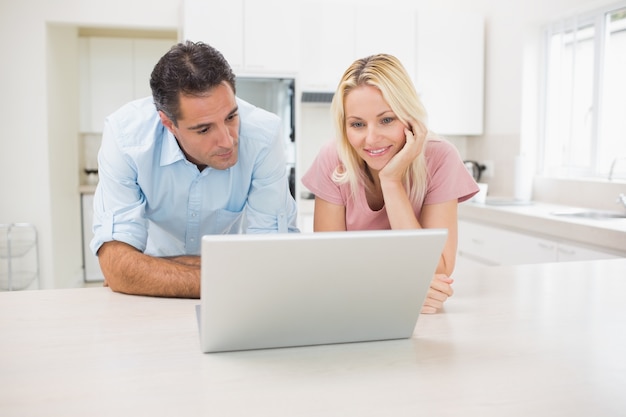 Casal sorridente usando laptop na cozinha