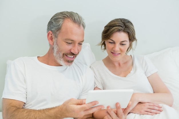 Casal sorridente usando tablet digital na cama no quarto
