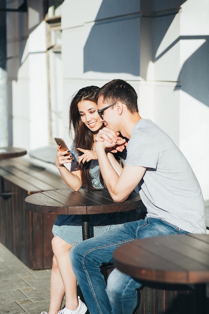 Casal sorridente usando telefone celular em um café ao ar livre