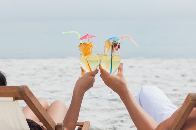 Casal taquilhando copos de cocktail na praia