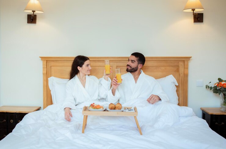Foto casal tilintando copos com suco na cama no quarto do hotel