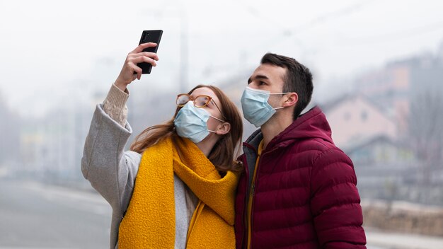 Casal tirando fotos usando smartphone com máscara médica