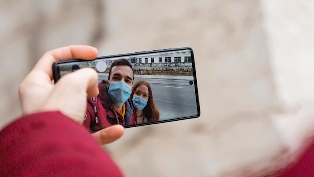 Foto casal tirando uma selfie junto com o smartphone usando máscaras médicas