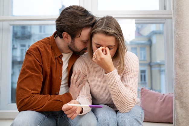 Casal triste de tiro médio com teste de gravidez