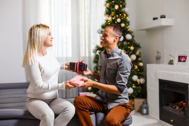 Casal trocando presentes de Natal perto da árvore de Natal.