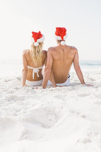 Casal usando chapéu de Papai Noel na praia