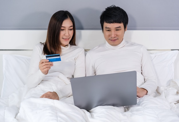 Casal usando computador portátil para compras on-line com cartão de crédito na cama