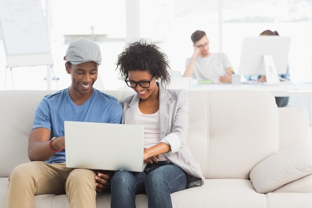 Foto casal usando laptop com colegas em segundo plano no escritório criativo