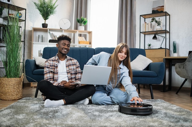 Foto casal usando laptop enquanto robô aspirador de carpete