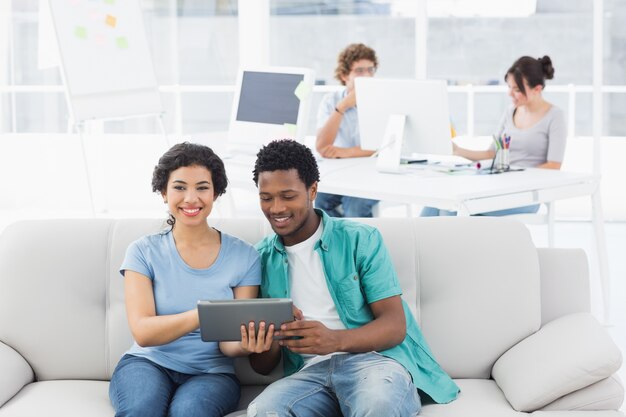 Casal usando tablet digital com colegas no escritório criativo