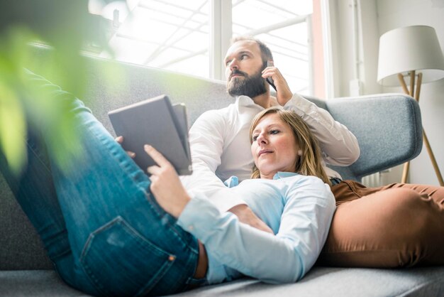 Casal usando tablet e celular no sofá