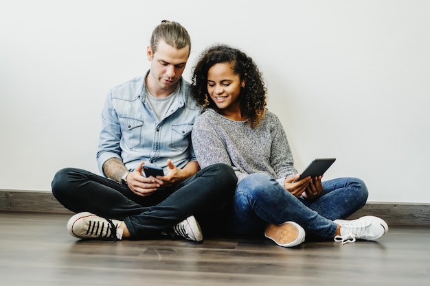 Foto casal usando tecnologias enquanto está sentado no chão em casa