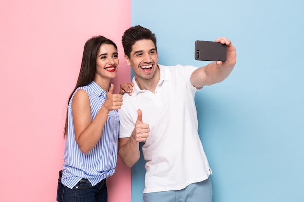 Foto casal usando telefone celular e tirando uma foto de selfie, isolada em uma parede colorida