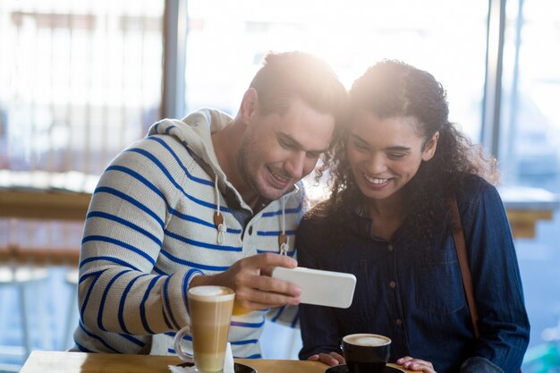 Casal usando telefone celular enquanto toma uma xícara de café