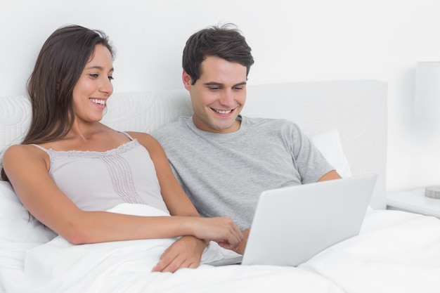 Casal usando um laptop juntos deitado na cama