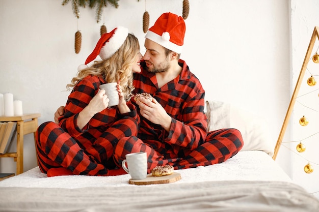 Casal vestindo pijama vermelho xadrez de natal sentado na cama