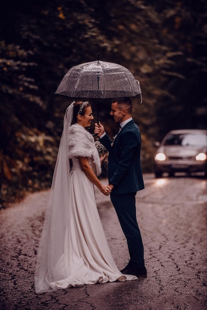Casamento momentos felizes. Um jovem casal feliz, recém-casados andando pelas ruas em tempo chuvoso enquanto carregava um guarda-chuva. foto de alta qualidade