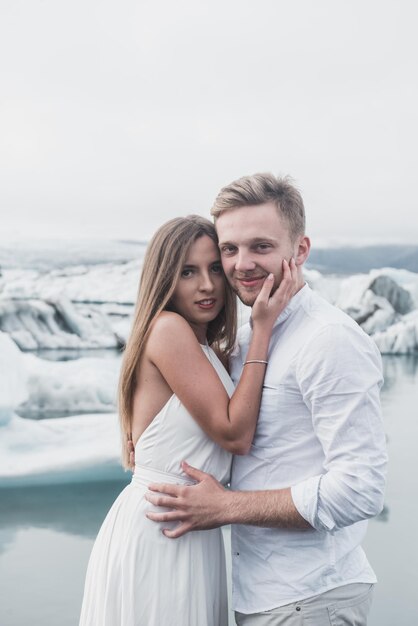 Casamento na islândia. um cara e uma garota de vestido branco estão se abraçando enquanto estão em um gelo azul