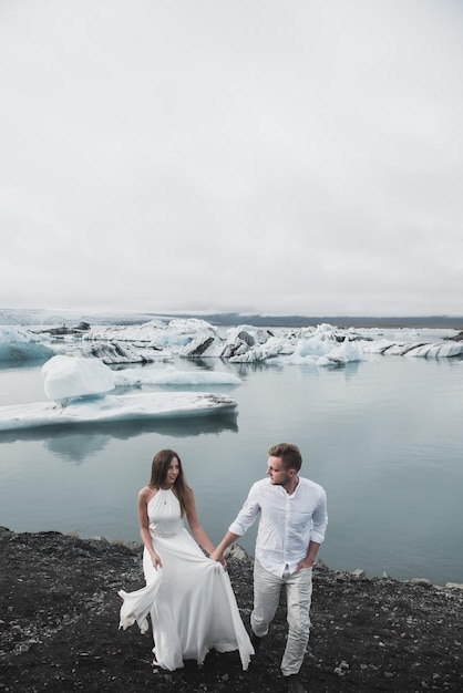 Casamento na Islândia. Um cara e uma garota de vestido branco estão se abraçando enquanto estão em um gelo azul