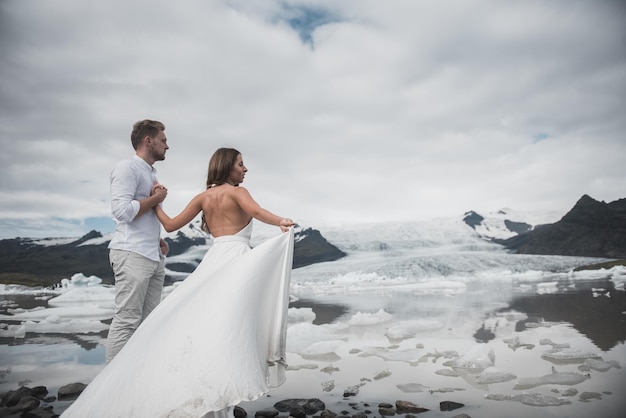 Casamento na Islândia. Um cara e uma garota de vestido branco estão se abraçando enquanto estão em um gelo azul