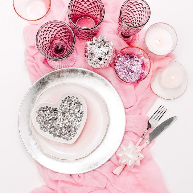 Casamento ou configuração de mesa festiva. Pratos, taças de vinho, velas e talheres com têxteis decorativos em fundo branco. Belo arranjo na cor rosa