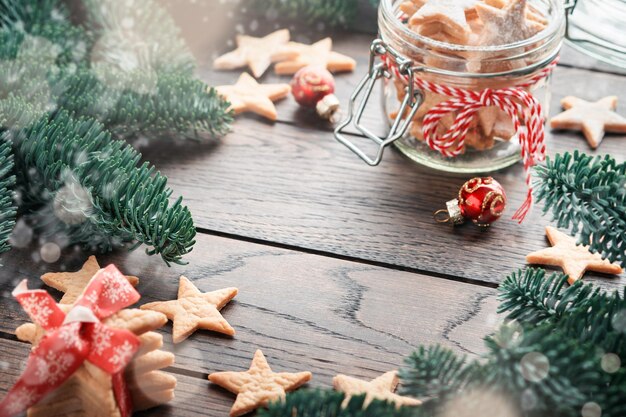 Casar com o fundo do Ano Novo de Natal com ramos de abeto e estrelas de biscoitos amanteigados de Natal com abeto de fita vermelha no lado direito e esquerdo no fundo escuro de madeira Vista superior Mock up