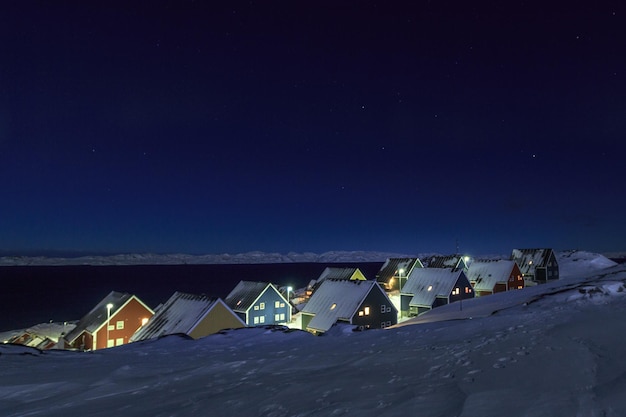 Casas inuit amarillas, azules, rojas y verdes cubiertas de nieve en el fiordo bajo el cielo estrellado de la ciudad de Nuuk en Groenlandia