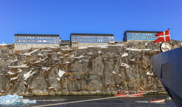 Casas Inuit azuis na rocha ao longo do fiorde com navios e barcos e bandeira da Dinamarca na popa da cidade de Nuuk, Gronelândia