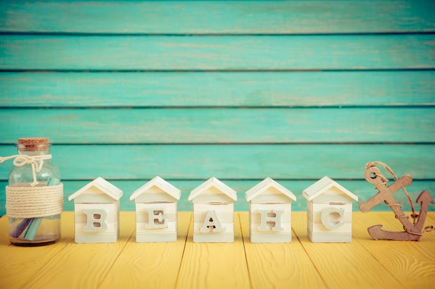 Casas de juguete de madera, botella de vidrio y ancla de madera sobre un piso de madera con fondo de pared de madera azul