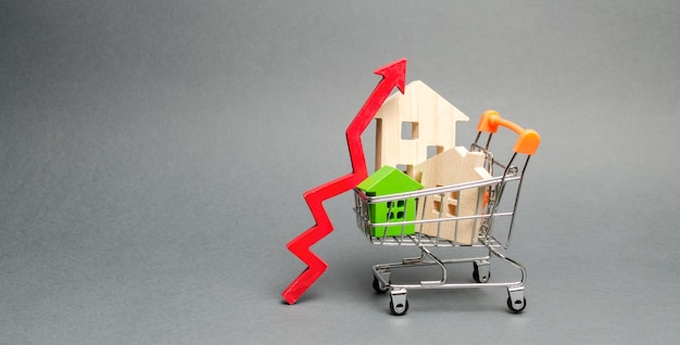 Foto casas de madera en un carrito de compras y flecha roja el concepto de aumento del costo de la vivienda