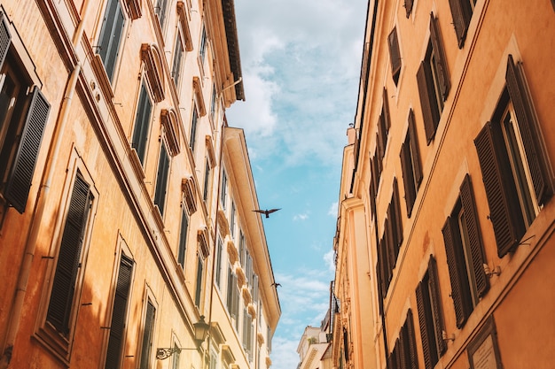 Casas romanas con contraventanas, cielo azul sobre la ciudad, pájaro vuela sobre una antigua calle en Roma, Italia.
