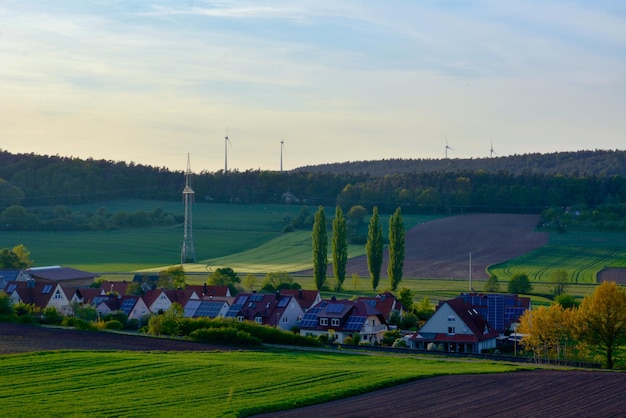 Casas rurais com painéis solares nos telhados. Os campos arados estão em primeiro plano. usinas de energia eólica