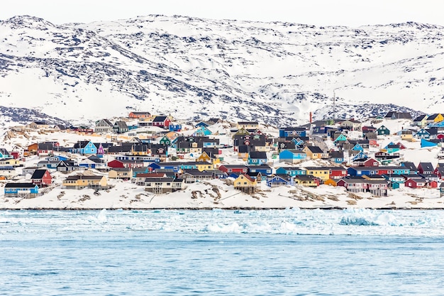 Casas vivas nas colinas rochosas cobertas de neve no fiorde da colorida cidade ártica Ilulissat Greenland