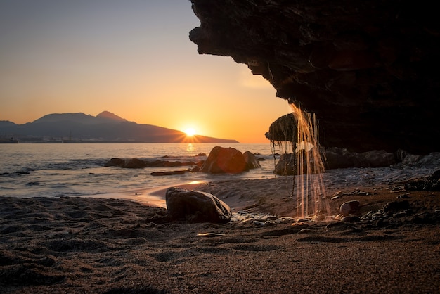 Cascada cayendo sobre una playa desde una piedra al atardecer. Costa de Ceuta en España.