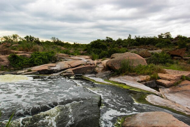 La cascada fluye entre rocas altas, piedras rojas y acantilados, arbustos y árboles verdes