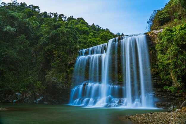 Foto una cascada está frente a una montaña con un cielo azul