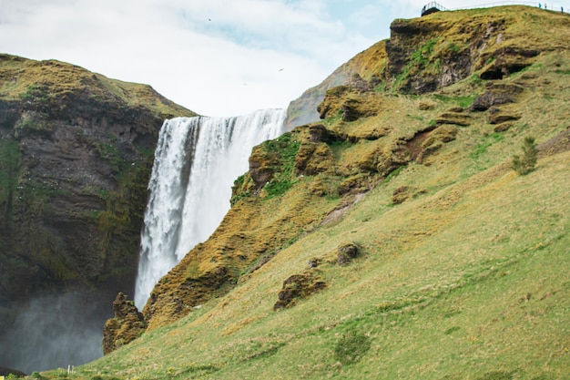 Foto una cascada en islandia con una mujer parada frente a ella.