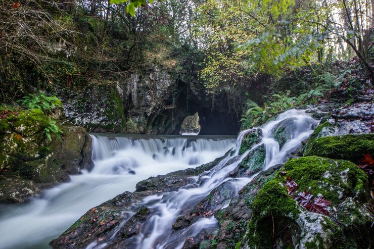 Foto cascada llena de rocas a los pies de una cueva al fondo