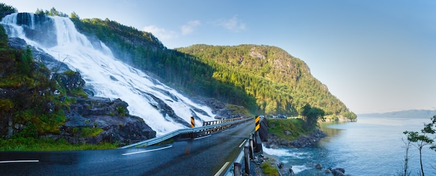 Cascada de montaña de verano en pendiente cerca de la carretera a lo largo del lago Sandvinvatnet (Noruega). Panorama.