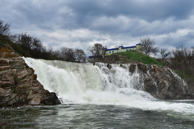 Una cascada tormentosa desde un acantilado de piedra Paisaje con agua en un día nublado Río hirviente