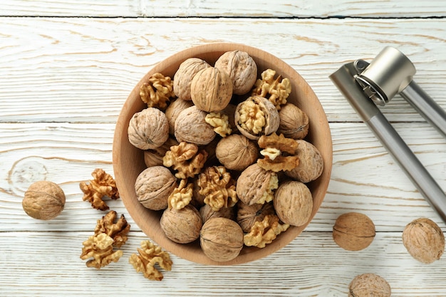 Cascanueces y tazón de nueces sobre fondo blanco de madera