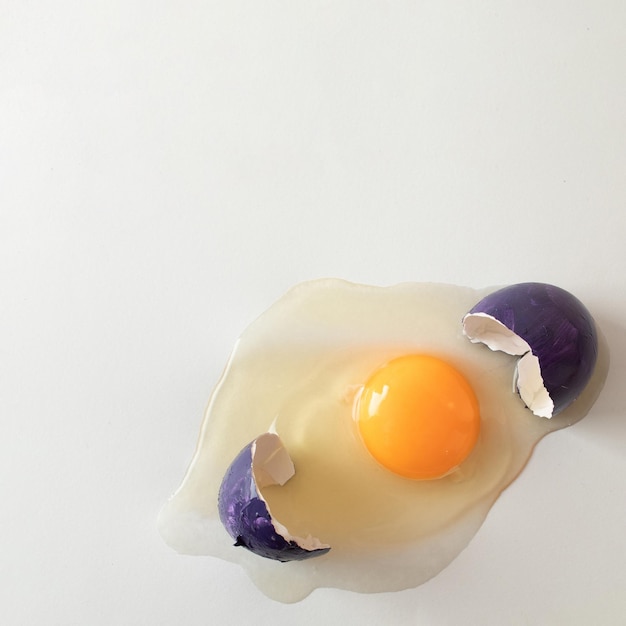 cáscara de huevo púrpura rota con huevo crudo espacio de copia creativa en fondo claro concepto minimalista de Pascua