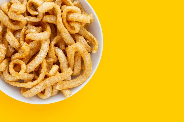 Cascas de porco crocantes fritas em chapa branca sobre fundo amarelo.