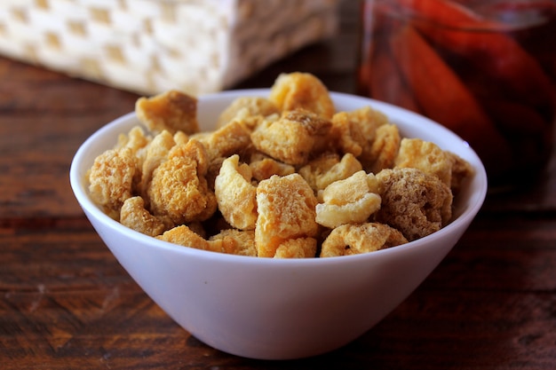 Foto cascas de porco (torresmo) frito em uma tigela de cerâmica na mesa de madeira rústica no restaurante. prato típico da culinária brasileira e asiática