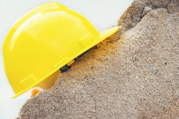 Casco amarillo y casa modelo de madera sobre una pila de arena