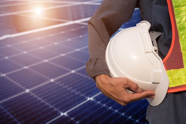 Casco blanco de seguridad en la mano y fondo borroso del panel de energía solar