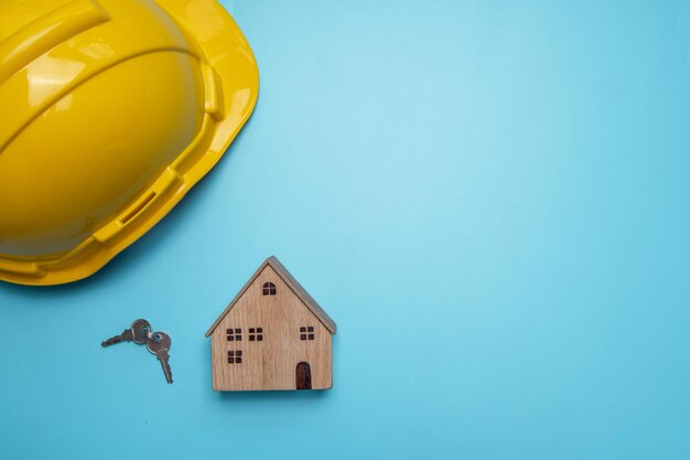 casco con casa de madera y llave en fondo azul concepto de bienes raíces