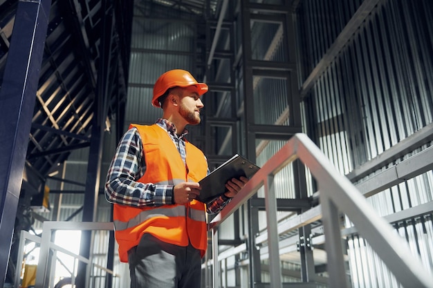 En casco de color naranja, trabajador de la construcción en uniforme está en la fábrica.