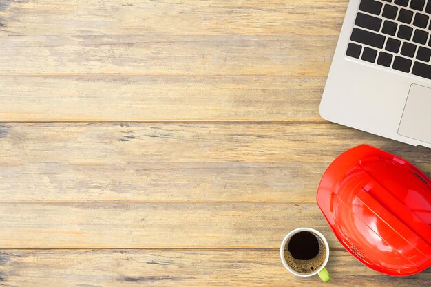 Casco de ingeniero de seguridad rojo, computadora portátil y taza de café en el fondo de la mesa de madera